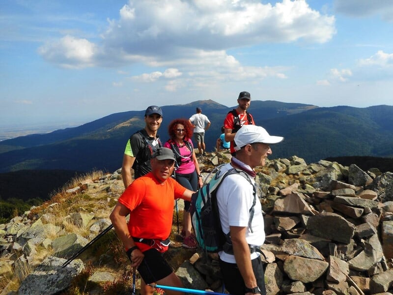 Groupe de randonneurs marchant sur un sentier rocheux en montagne sous un ciel bleu.