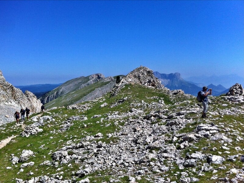 Personnes en randonnée sur un chemin rocheux en montagne avec un ciel bleu et des sommets en arrière-plan.