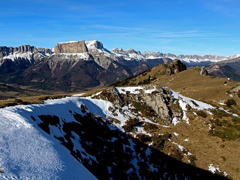 Paysage de montagne avec des sommets enneigés et des prairies sous un ciel bleu clair.