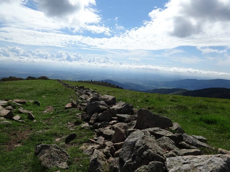 Chemin de randonnée en montagne avec des rochers et de l'herbe verte sous un ciel partiellement nuageux.