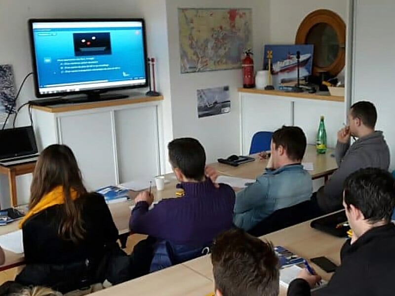 Des personnes assistent à un cours en salle avec un écran montrant une présentation sur le permis bateau.