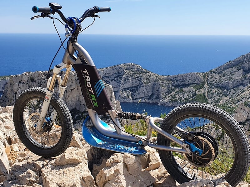 Trottinette électrique tout-terrain sur un rocher avec vue sur la mer et falaises escarpées sous un ciel bleu clair.