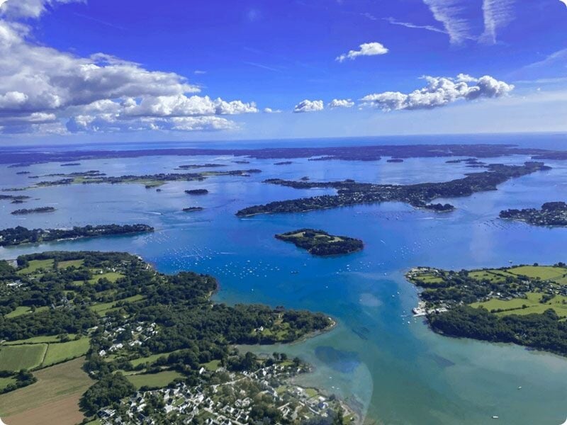 Vue aérienne du golfe du Morbihan avec ses nombreuses îles et la côte verdoyante sous un ciel partiellement nuageux.
