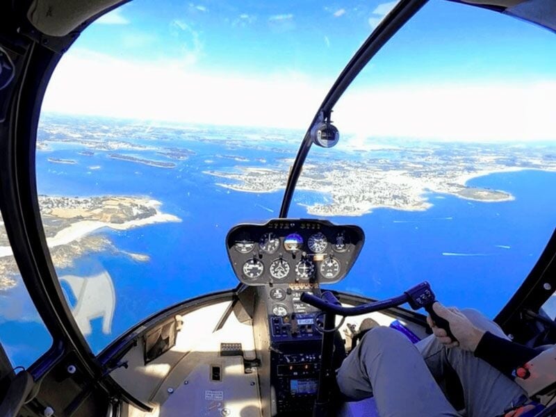 Intérieur du cockpit d'un hélicoptère avec vue sur le pilote et le paysage maritime du golfe du Morbihan.