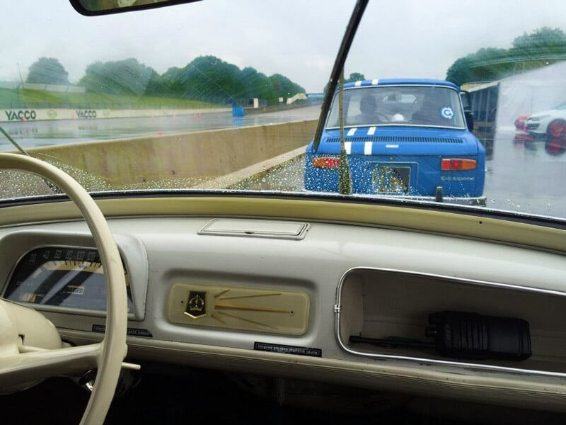 Vue depuis l'intérieur d'une voiture ancienne sur une piste de course avec une autre voiture bleue devant.