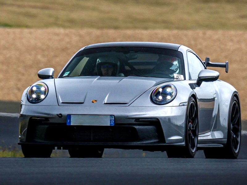 une porsche 992 GT3 de couleur grise sur une piste asphalte avec un champ de blé en fond