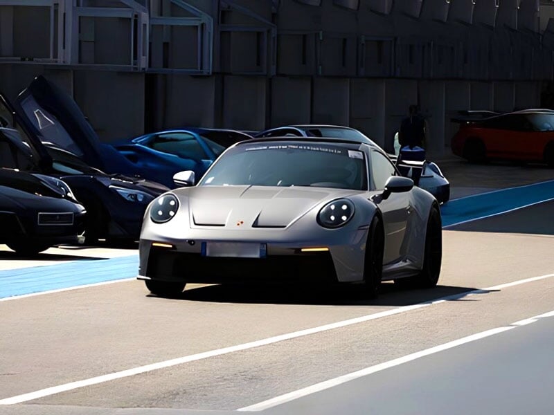 une porsche grise roule en bord de piste devant d'autres voitures de sport
