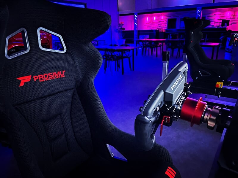     Gros plan d'un siège baquet de simulateur Prosimu avec un volant Fanatec, éclairé par une lumière ambiante bleue dans une salle dédiée aux simulateurs.