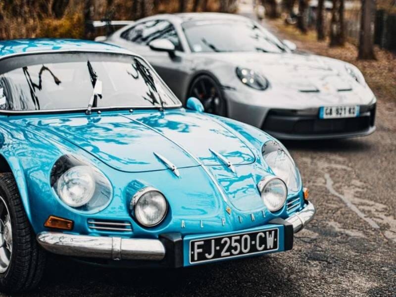 Deux voitures de sport garées sur une route bordée d'arbres en hiver, une bleue et une grise en arrière-plan, prêtes pour une balade dans Paris.