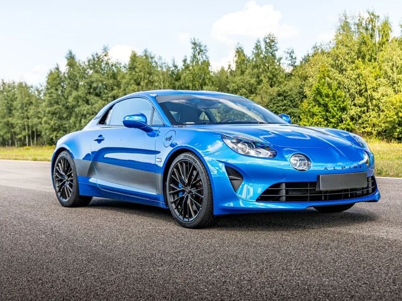 Voiture de sport bleue garée sur une piste avec un arrière-plan d'arbres verts sous un ciel partiellement nuageux.