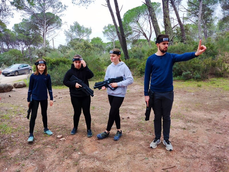 Quatre personnes en tenue décontractée avec casques et pistolets laser participent à un jeu en forêt.