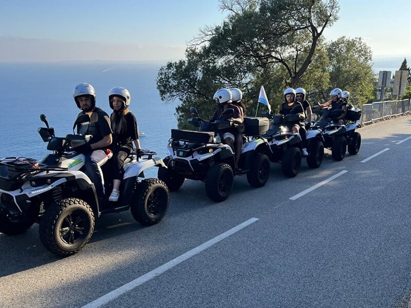 Alignement de quads avec des participants portant des casques, garés le long d'une route surplombant la mer.