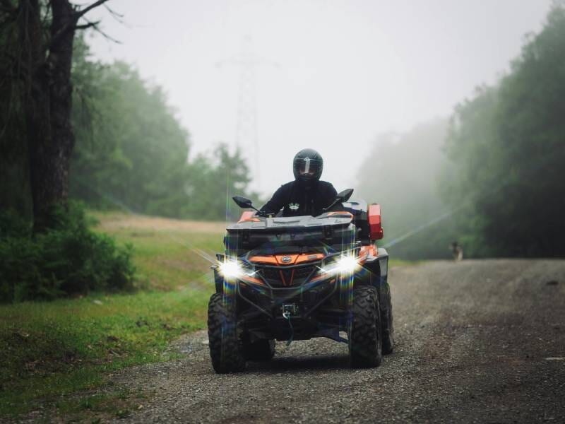 Personne en casque conduisant un quad tout-terrain sur un chemin de forêt brumeux lors d'une randonnée près du Tréport.
