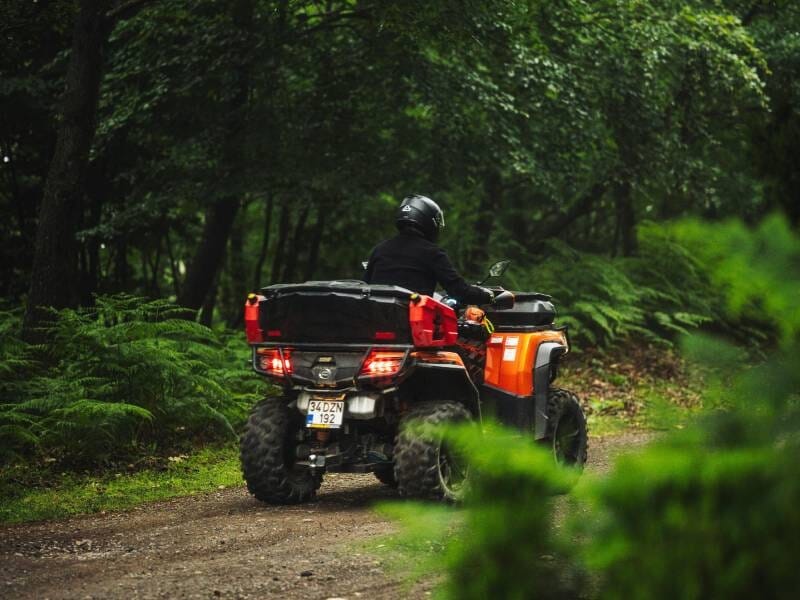 Conducteur de quad orange avec casque roulant sur un sentier forestier entouré de verdure dense.