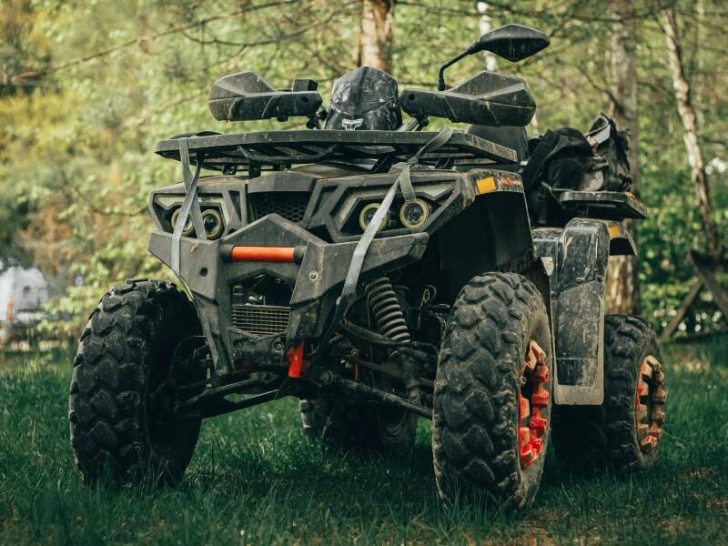 Quad tout-terrain noir et orange garé sur l'herbe dans une forêt avec des arbres en arrière-plan.