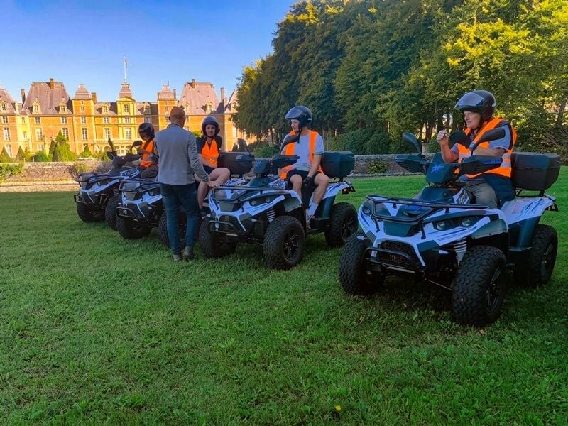 Personnes en gilets orange discutant près de quads stationnés sur une pelouse verte avec un château en arrière-plan.