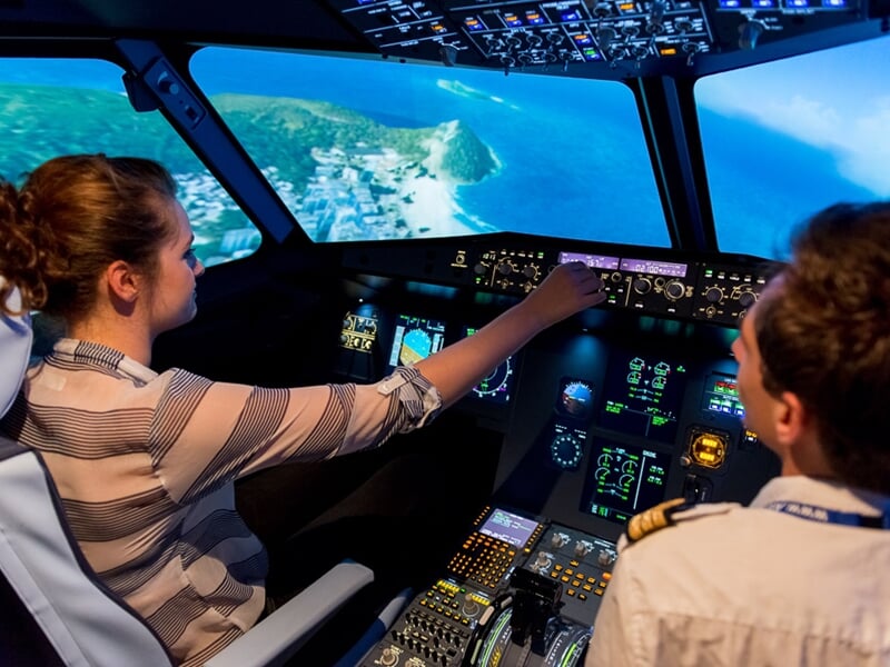 Une femme et un homme en uniforme de pilote dans un simulateur d'avion, la femme manipulant les commandes de vol.