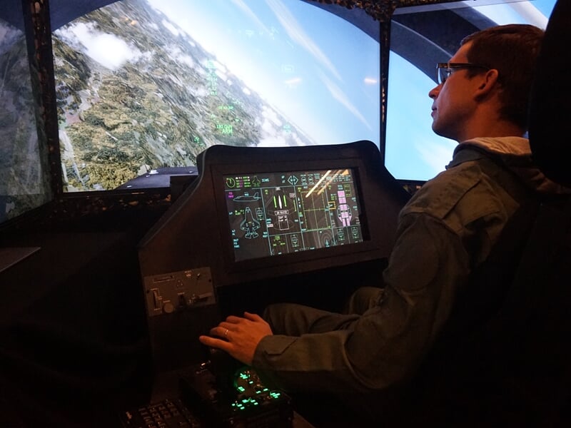 Homme concentré dans un simulateur de pilotage d'avion, manipulant les commandes avec un affichage numérique devant lui.