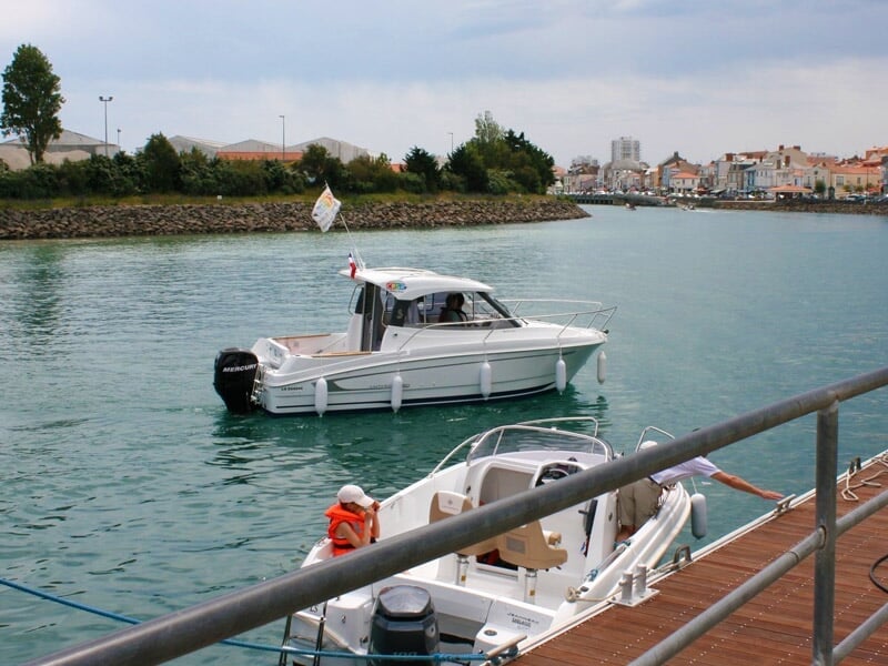Bateau blanc amarré près d'un quai en bois avec un paysage urbain et des arbres en arrière-plan.