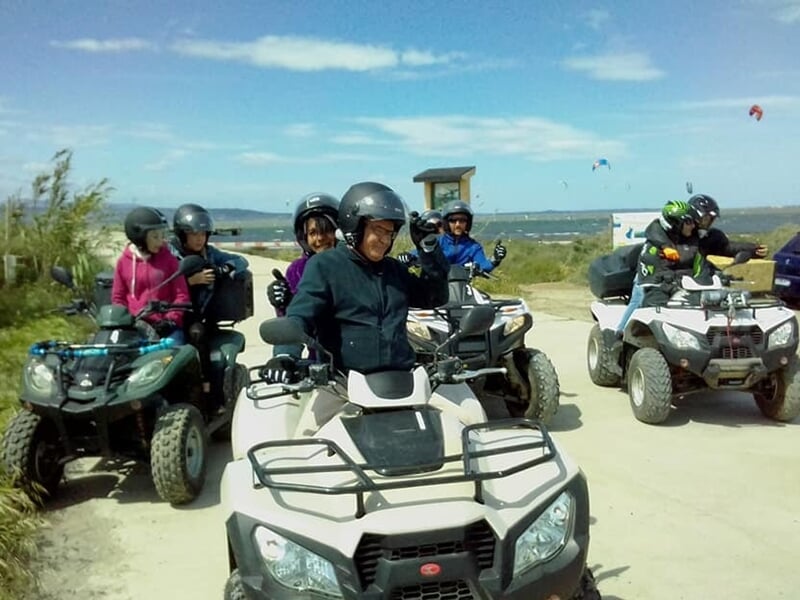 Groupe de personnes en casque sur des quads stationnés sur un terrain clair avec un ciel bleu et des montagnes au loin.