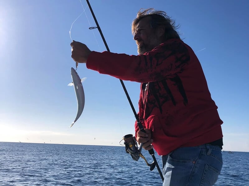 Homme en veste rouge pêchant en mer, tenant une canne à pêche avec un petit poisson accroché.