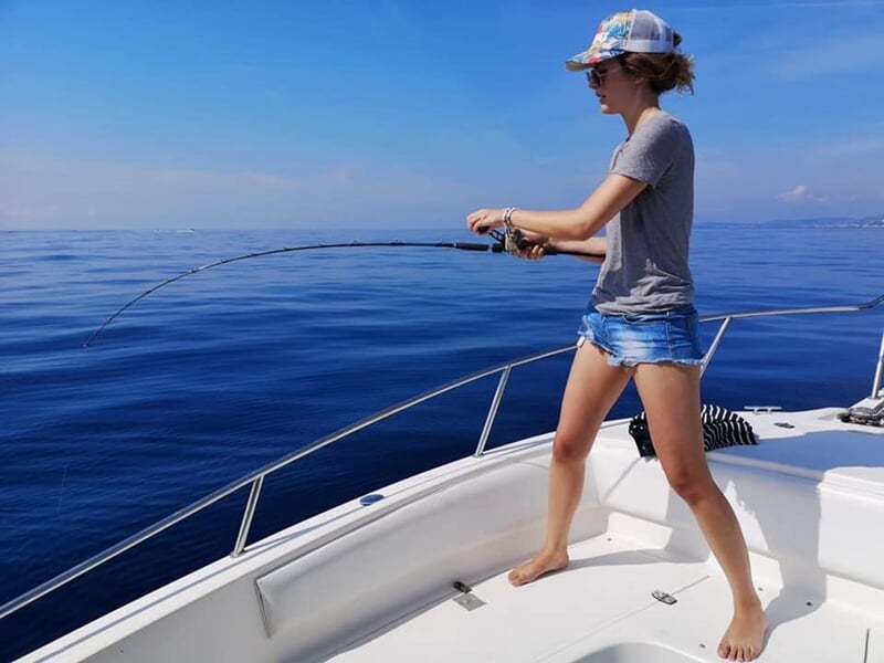 Jeune femme en short et casquette pêchant debout sur un bateau en pleine mer par temps clair.
