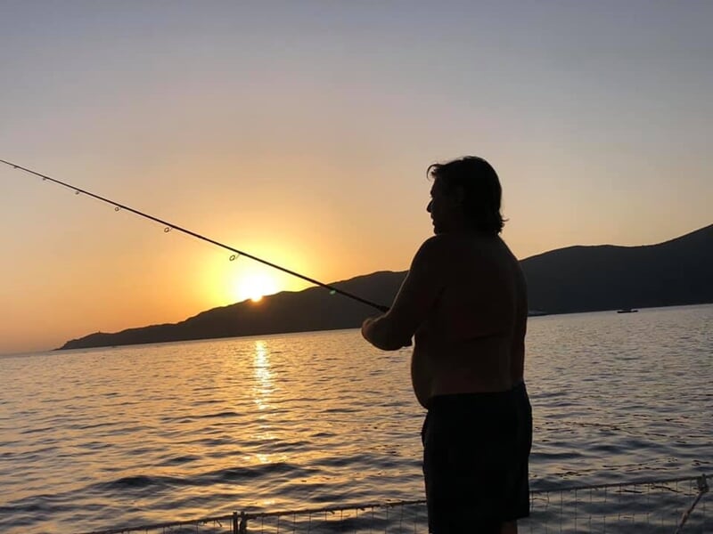 Personne pêchant au coucher du soleil sur un bateau, silhouette contre un ciel orangé et mer calme.