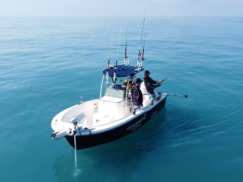 Bateau de pêche au gros sur une mer calme avec deux pêcheurs en action sous un ciel dégagé.