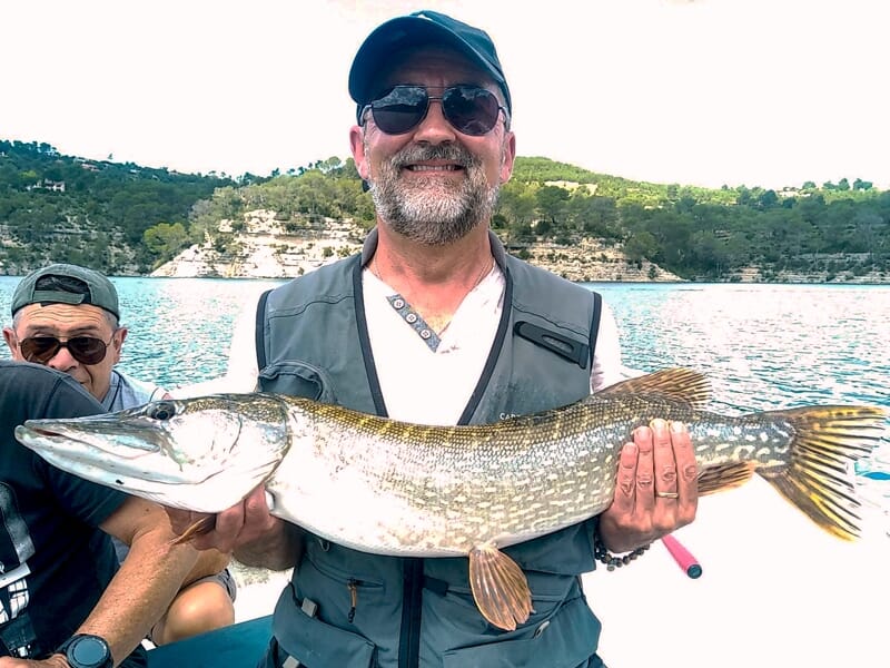 Pêcheur heureux avec lunettes de soleil montrant un brochet capturé sur un bateau au milieu d'un lac