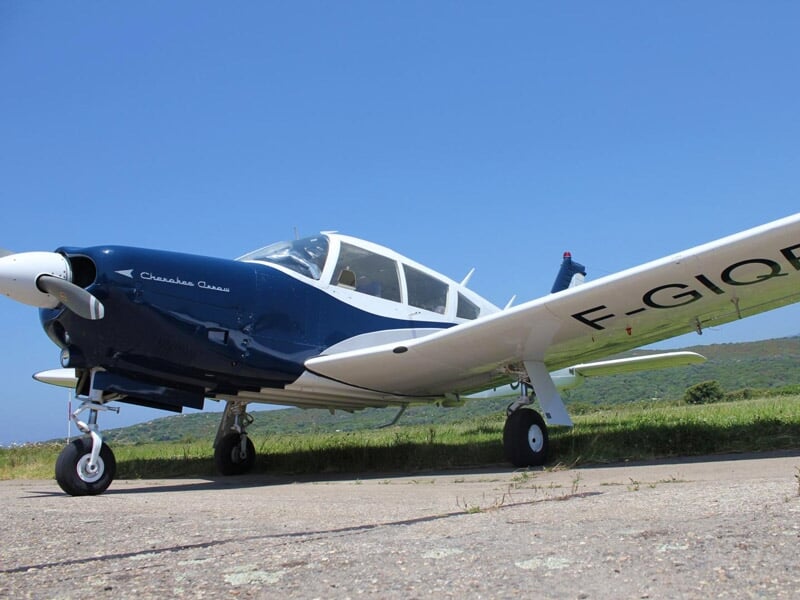 Avion léger blanc et bleu immatriculé F-GIQR stationné sur un terrain avec ciel bleu en arrière-plan.