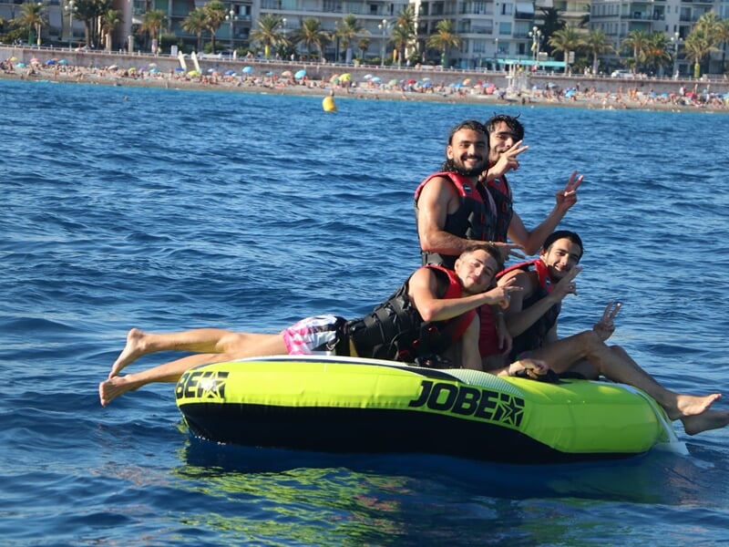 Groupe de quatre amis posant joyeusement sur une bouée tractée verte flottant sur l'eau bleue à Nice.