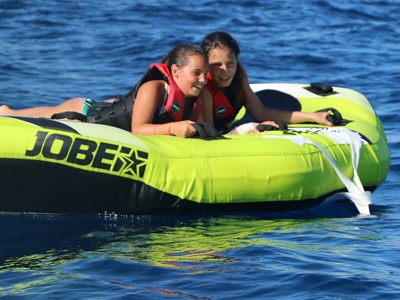 Deux jeunes femmes souriantes sur une bouée tractée verte, profitant d'une activité nautique à Nice.
