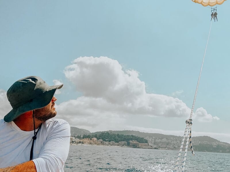 Homme en chapeau regardant vers le ciel en mer, avec un parachute ascensionnel visible dans le ciel bleu.