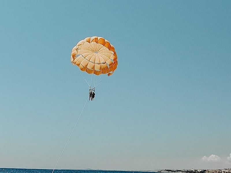 Personne en parachute ascensionnel orange flottant haut dans le ciel au-dessus de la mer à Nice.