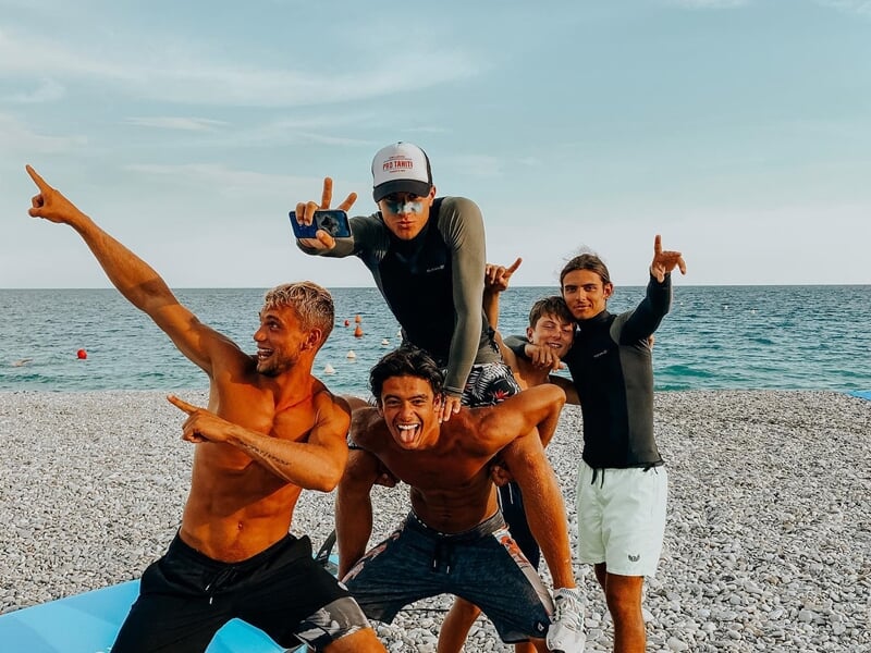 Groupe de jeunes posant joyeusement sur une plage de galets avec la mer en arrière-plan à Nice.