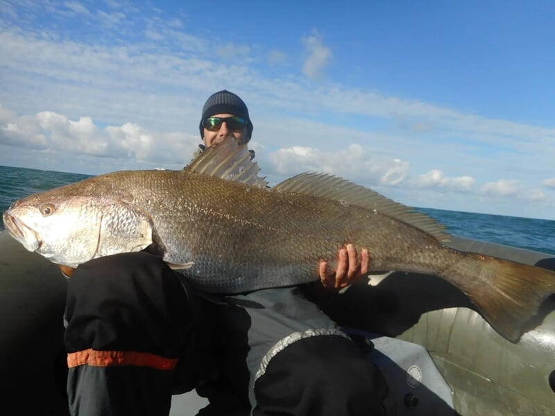 Pêcheur assis dans un bateau gonflable tenant un très gros poisson sous un ciel partiellement nuageux.