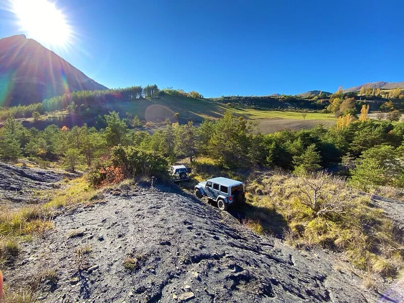 Deux 4x4 dans un paysage de collines verdoyantes sous ciel bleu, soleil éclatant à gauche