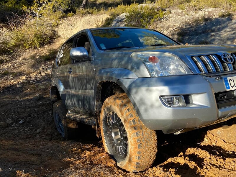 SUV gris avec roues couvertes de boue grimpant un sentier forestier en pente
