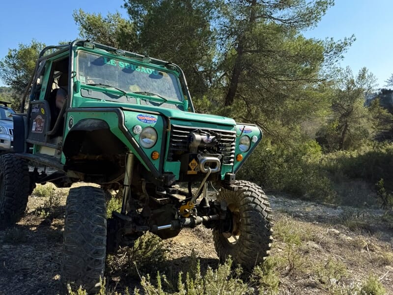 4x4 vert équipé d’un treuil avant arrêté sur sentier forestier entouré d’arbustes et pins