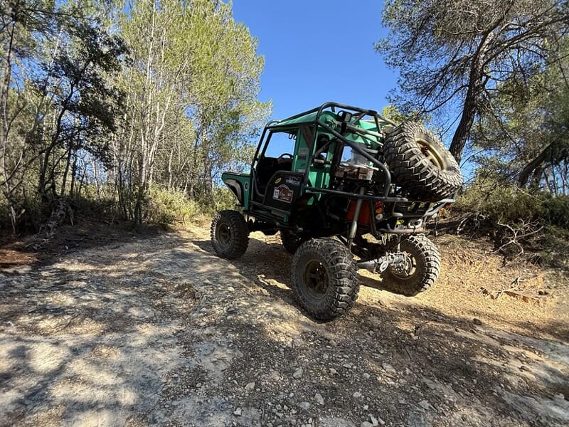 4x4 vert de dos montant un chemin rocailleux en forêt avec roue de secours fixée à l’arrière