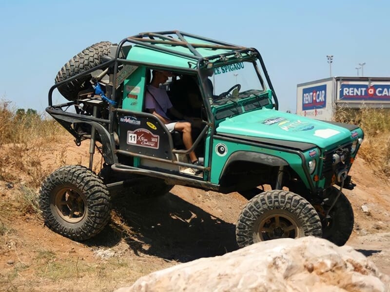 Voiture 4x4 verte en pleine montée sur un terrain accidenté avec un conducteur concentré au volant.