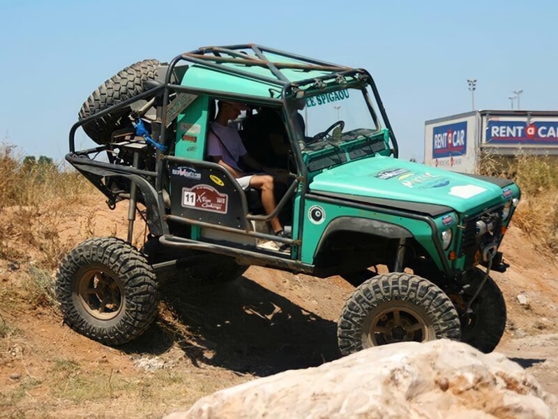 Voiture 4x4 verte en pleine montée sur un terrain accidenté avec un conducteur concentré au volant.