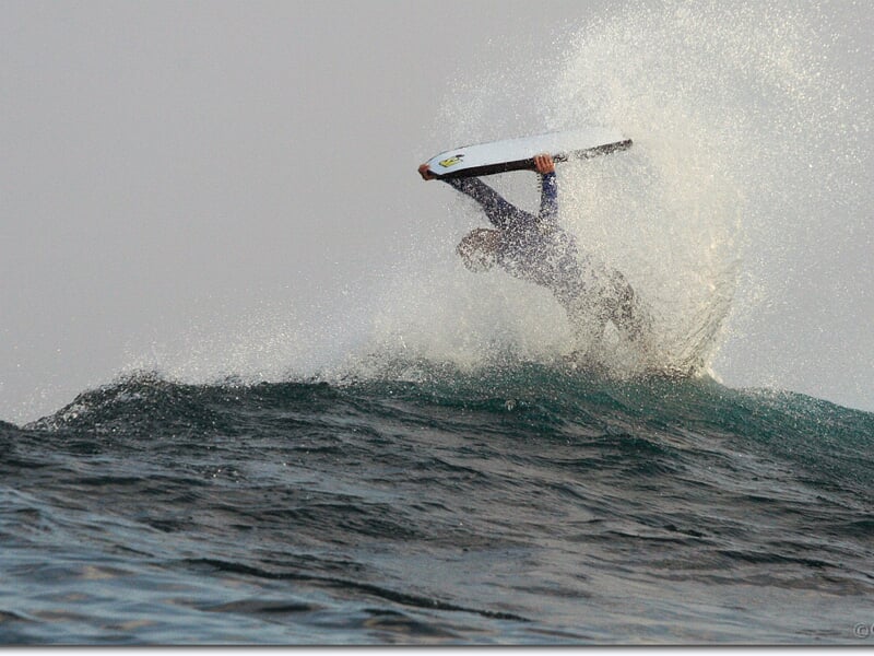 Surfeur effectuant une figure acrobatique avec sa planche sur une vague éclaboussante.