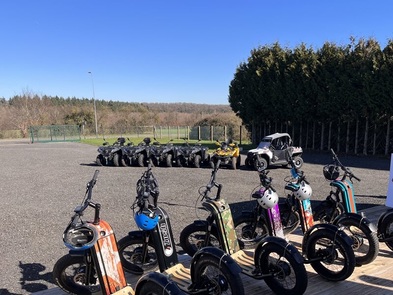 Plusieurs trottinettes électriques stationnées sur un terrain avec des casques posés dessus, prêtes à être utilisées.