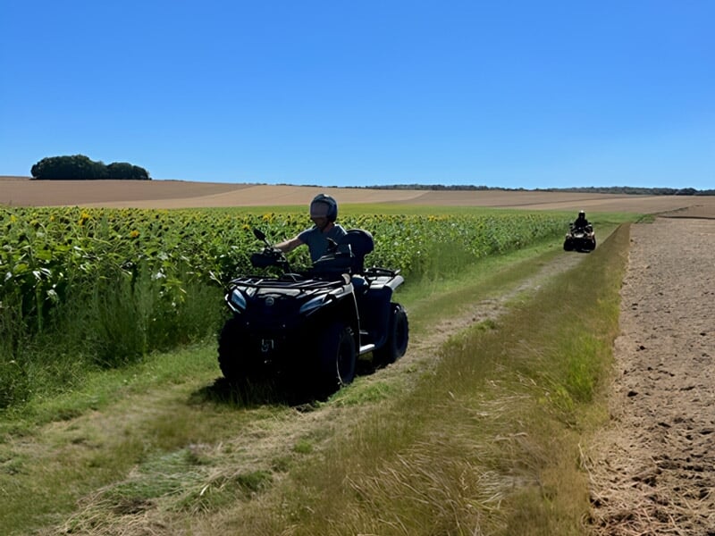 Deux quads roulant sur un chemin entre des champs cultivés sous un ciel bleu lumineux.