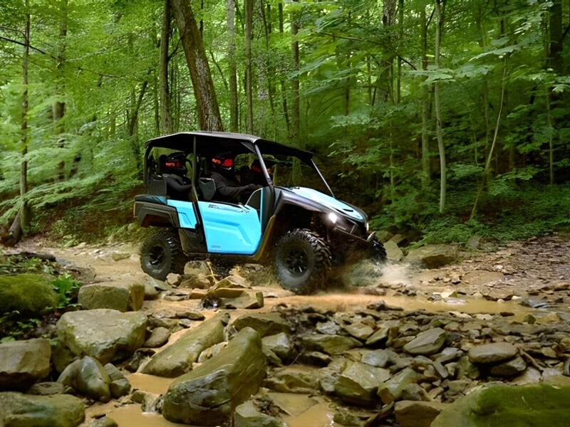 Quad bleu clair traversant un ruisseau rocheux dans une forêt dense et verdoyante.