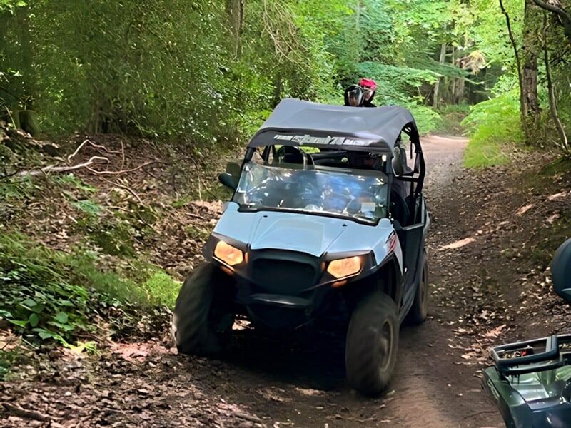 Quad noir avec conducteur portant un casque rouge roulant sur un chemin forestier ombragé.