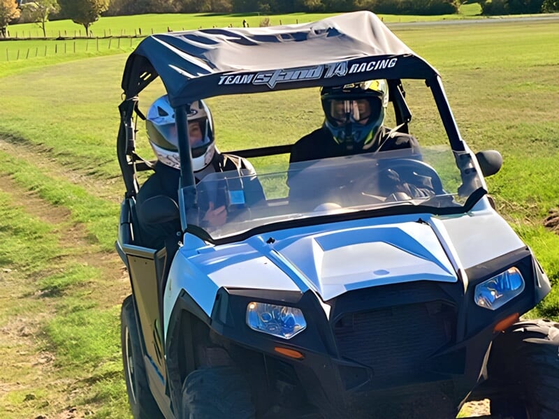 Deux personnes en quad blanc avec casques, roulant sur un chemin de campagne ensoleillé.