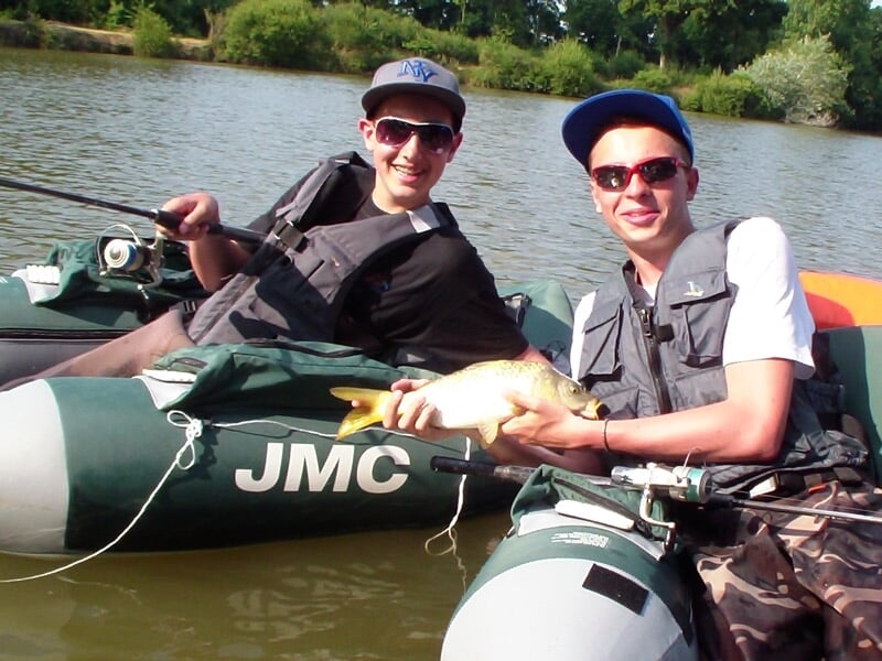Deux adolescents souriants assis sur des float tubes sur un lac, tenant un poisson jaune entre eux.