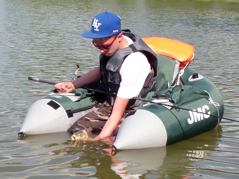 Jeune garçon en float tube relâchant un poisson dans l'eau, portant un gilet de sauvetage et une casquette.